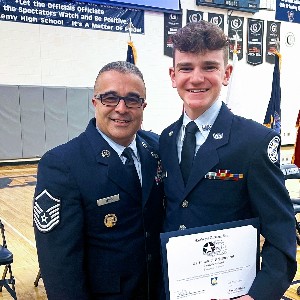 Student in uniform holds his award certificate and smiles at the camera with his instructor